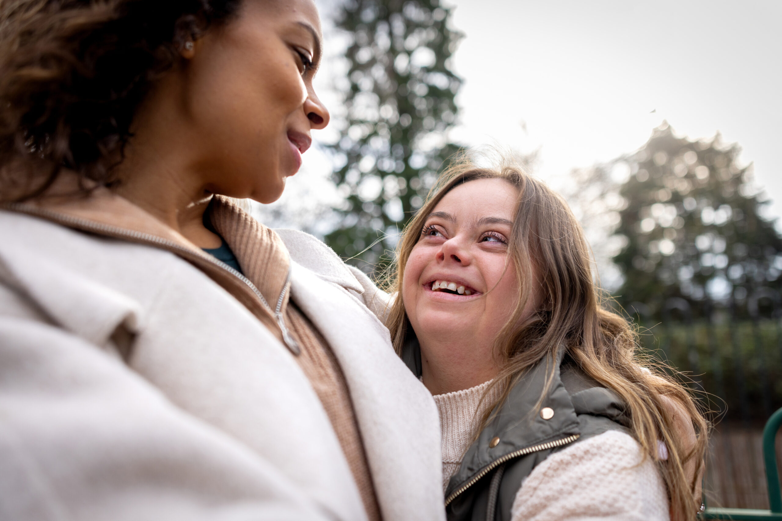 Close-up of a woman with her sister who has Down syndrome smiling at each other face to face. They are both wearing warm clothing on a cold winter morning. The park is located in Gateshead.